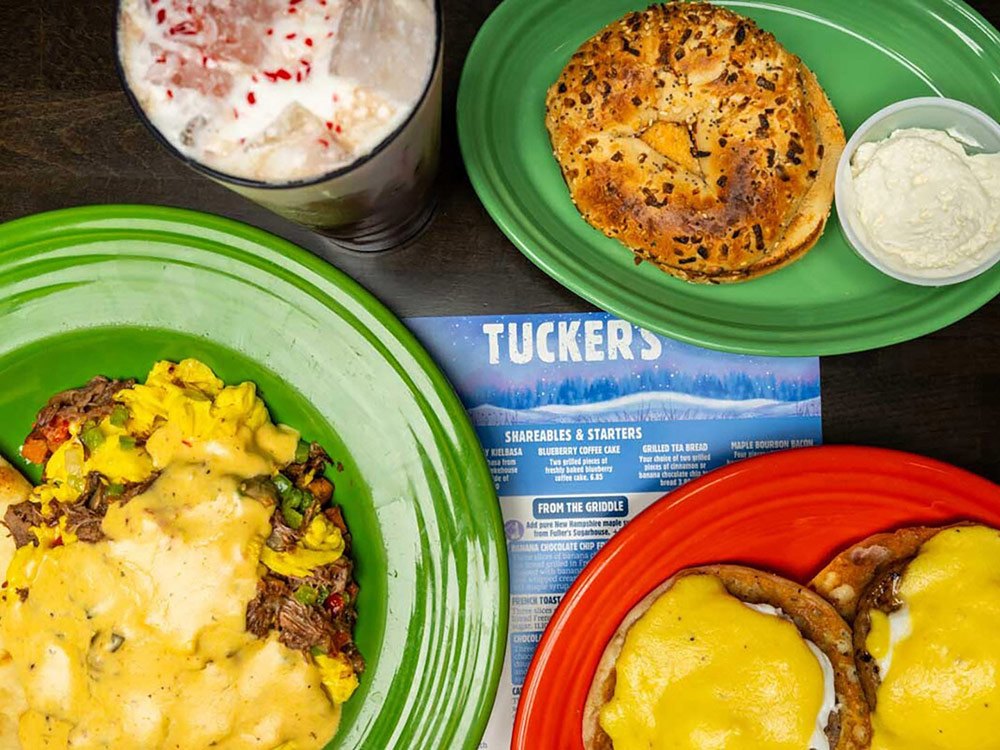 Eggs Benedict, scrambled eggs with cheese, an everything bagel with cream cheese, and a milkshake on a table.