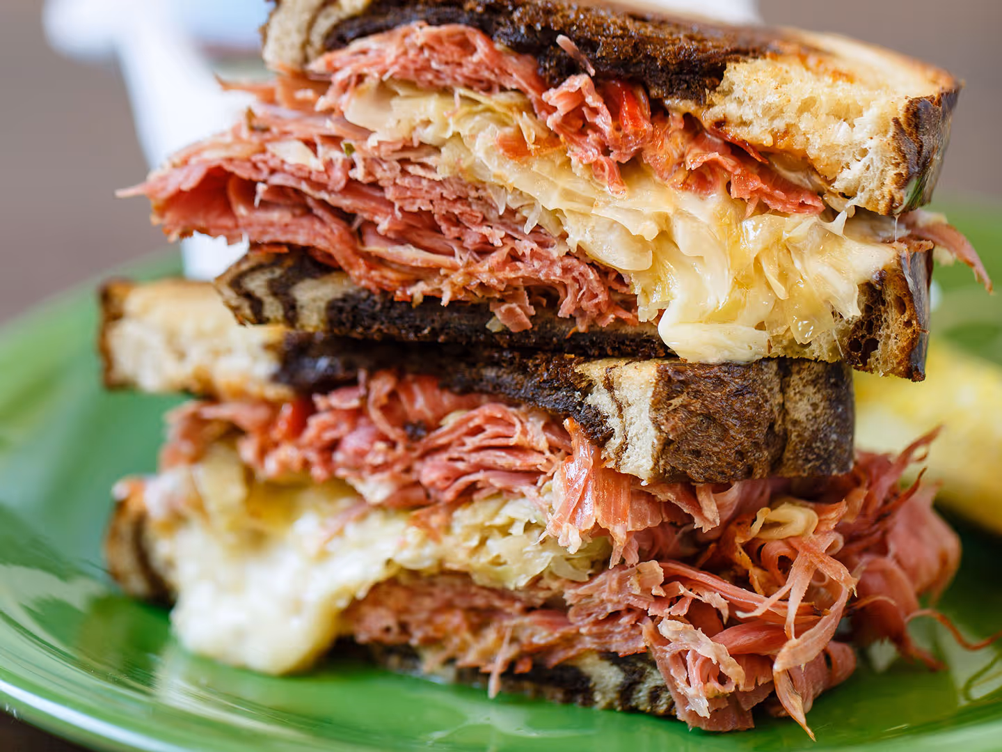 A stacked corned beef and sauerkraut sandwich on toasted rye bread, served on a green plate.