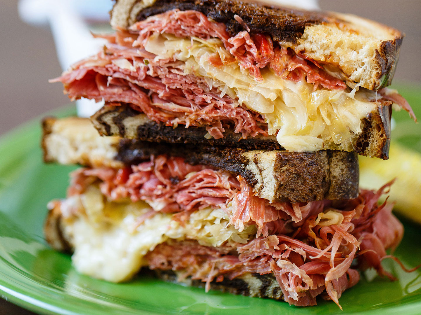 A stacked corned beef and sauerkraut sandwich on toasted rye bread, served on a green plate.