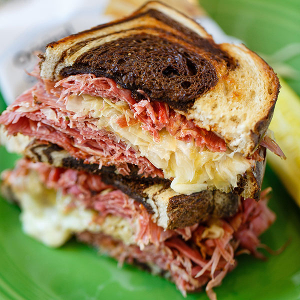 A stacked corned beef and sauerkraut sandwich on toasted rye bread, served on a green plate.