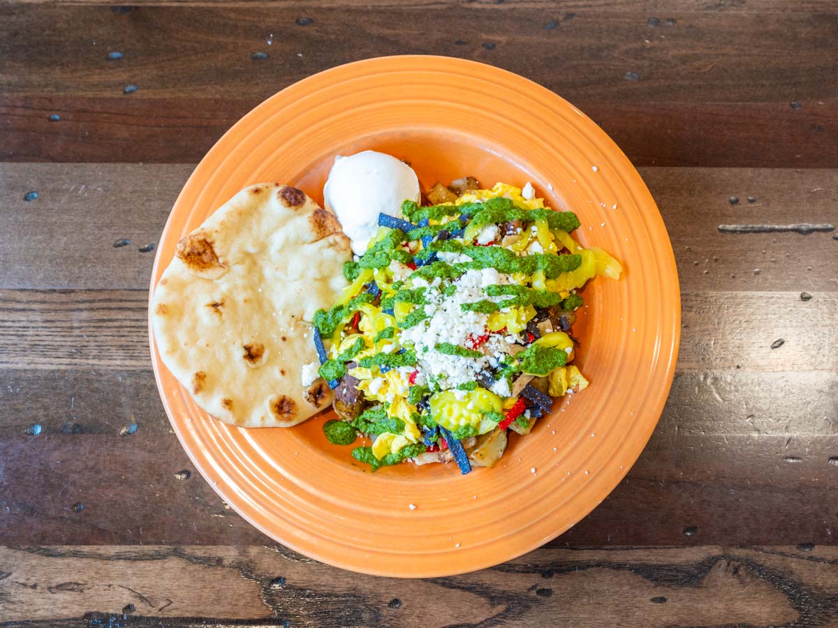 Eggs Benedict, scrambled eggs with cheese, an everything bagel with cream cheese, and a milkshake on a table.