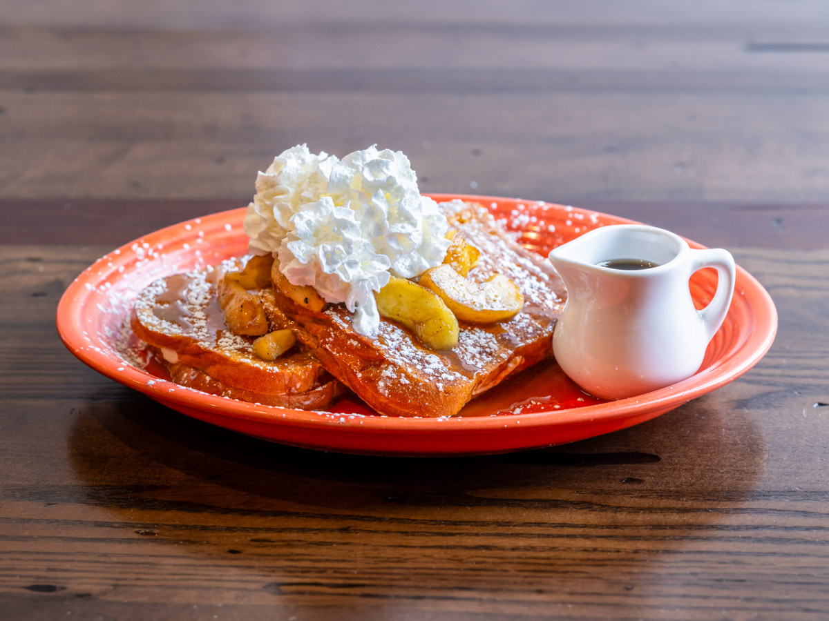 Three slices of French toast topped with blueberries, powdered sugar, and icing on a green plate with syrup on the side.
