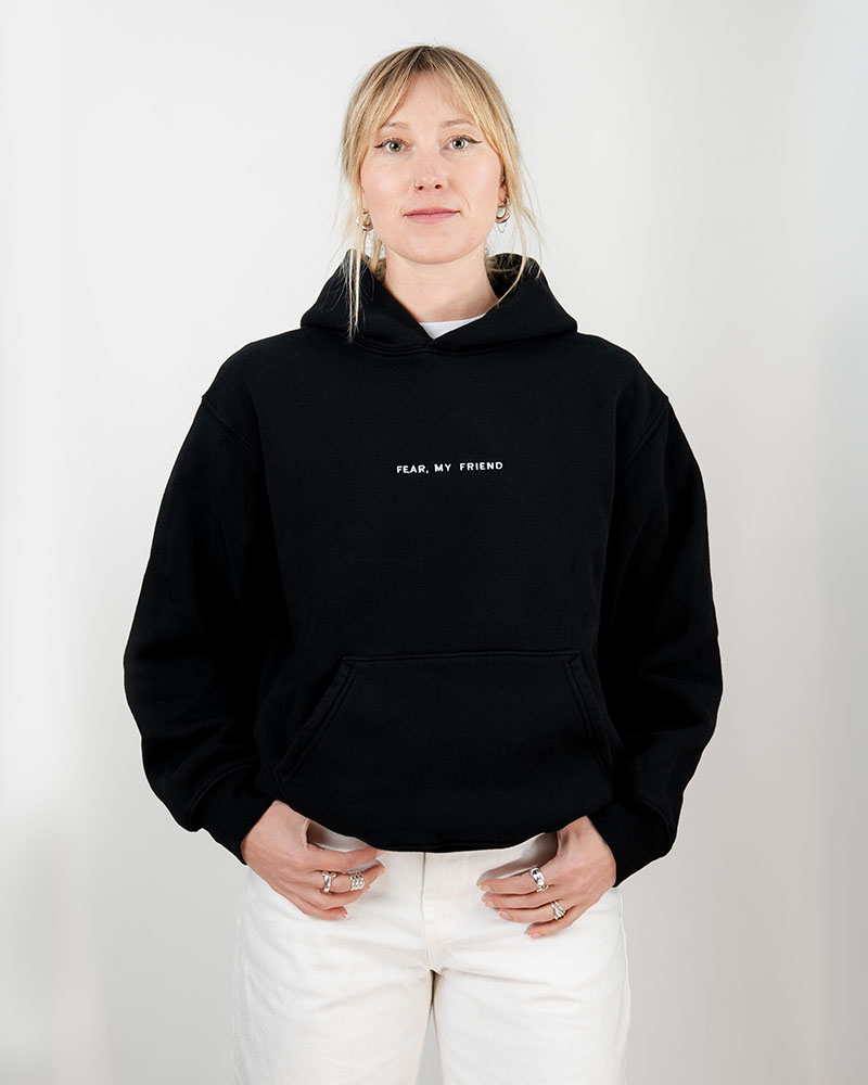 A woman with blonde hair wearing a black sweater with the words fear my friend written in white on the front