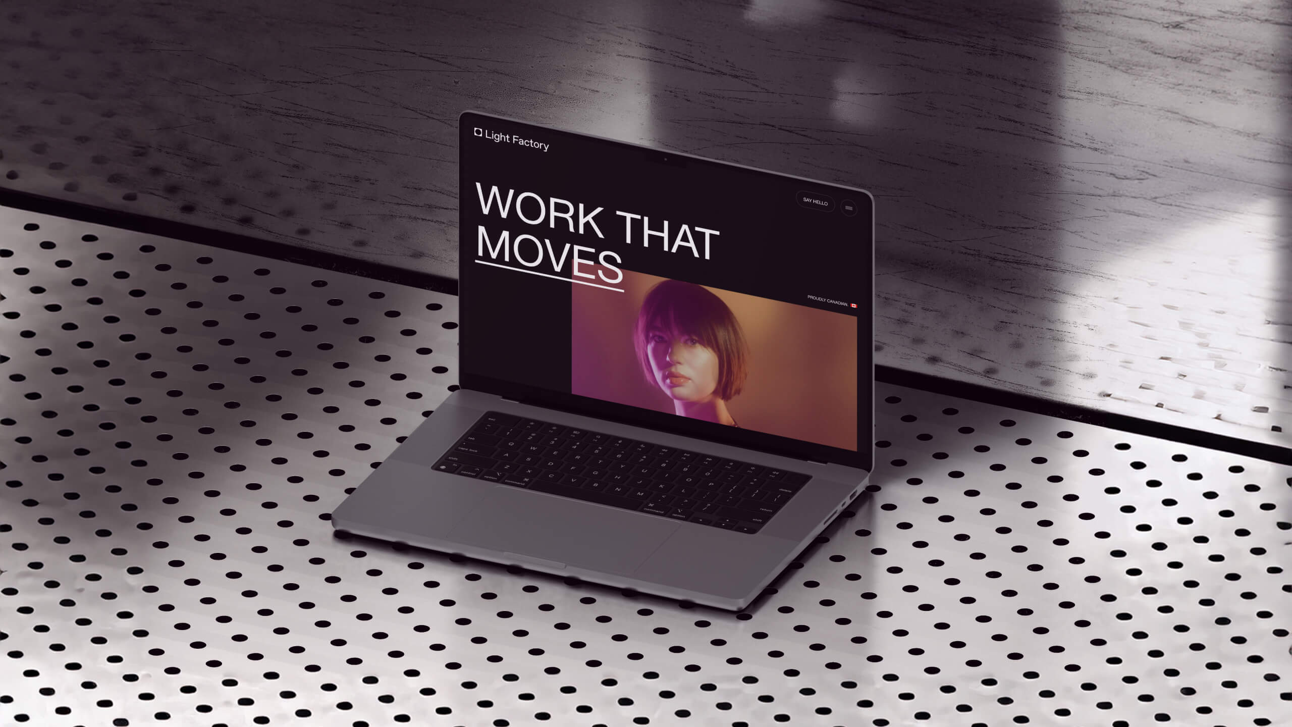Open laptop on perforated metal table displaying a website with text 'WORK THAT MOVES' and a woman's portrait.