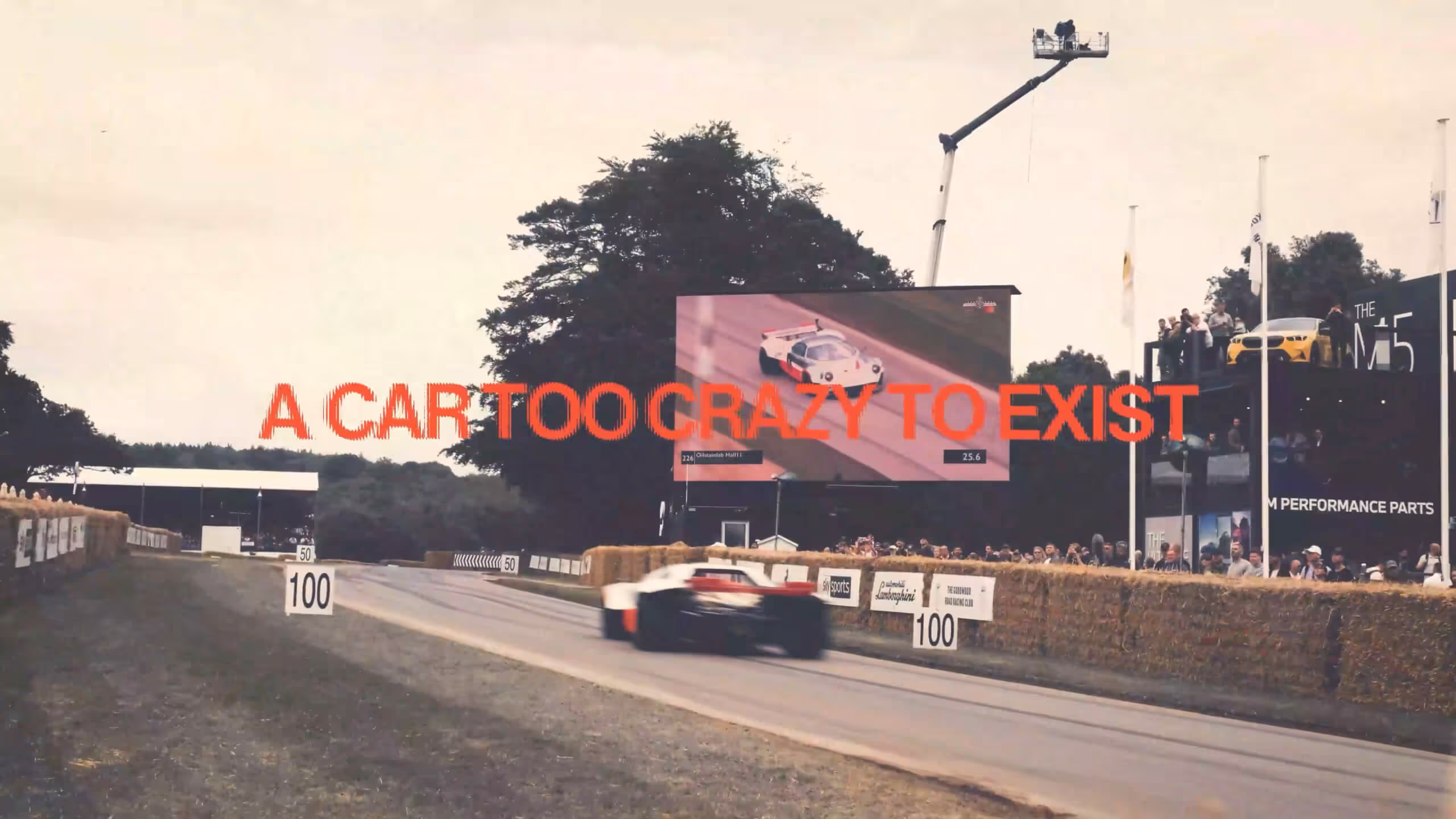 Race car speeding on a track with hay bales and a large screen showing another race car.