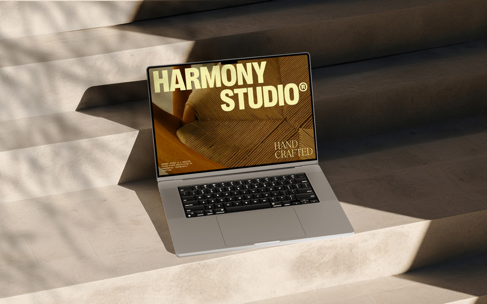 Laptop on stone steps displaying 'Harmony Studio Hand Crafted' with an image of a textured chair.