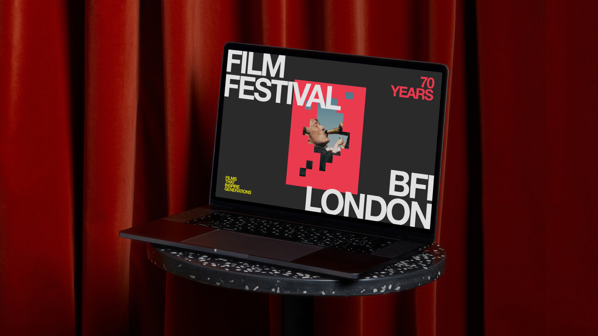 Laptop on round table shows BFI London Film Festival 70 years poster with man shouting in megaphone.