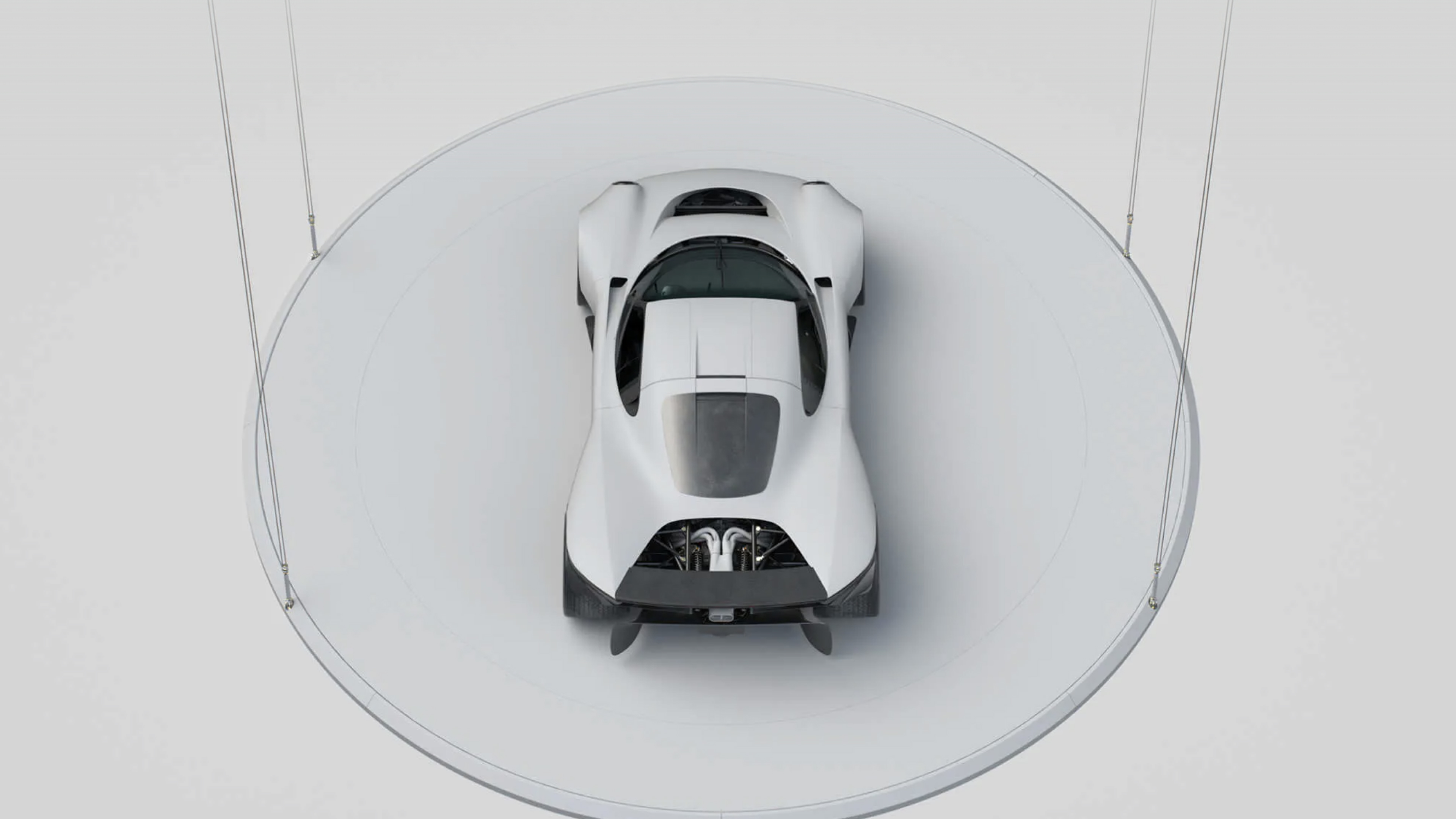 Top-down view of a sleek white sports car on a circular platform with cables attached.