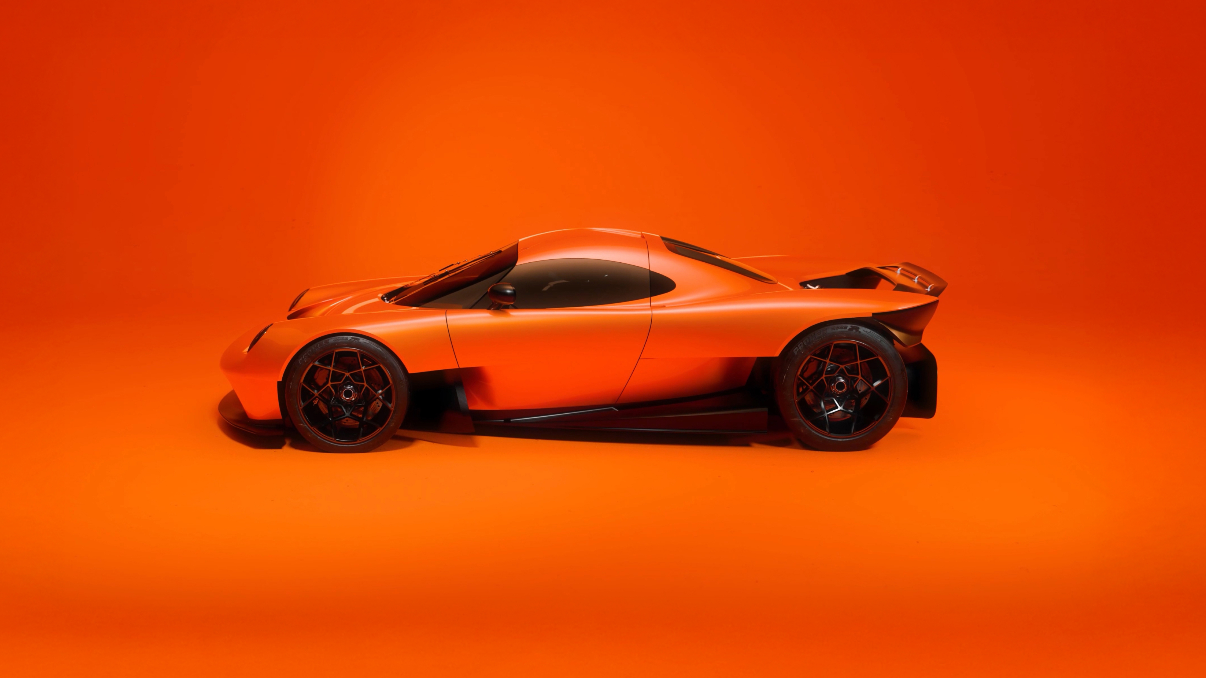 Sleek orange sports car with black wheels on an orange background in side profile view.