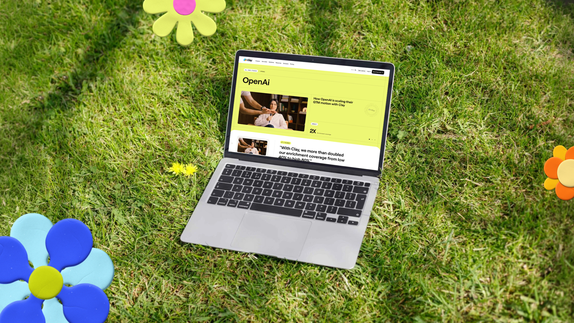 Laptop on grass showing a webpage about OpenAI with colorful cartoon flowers nearby.