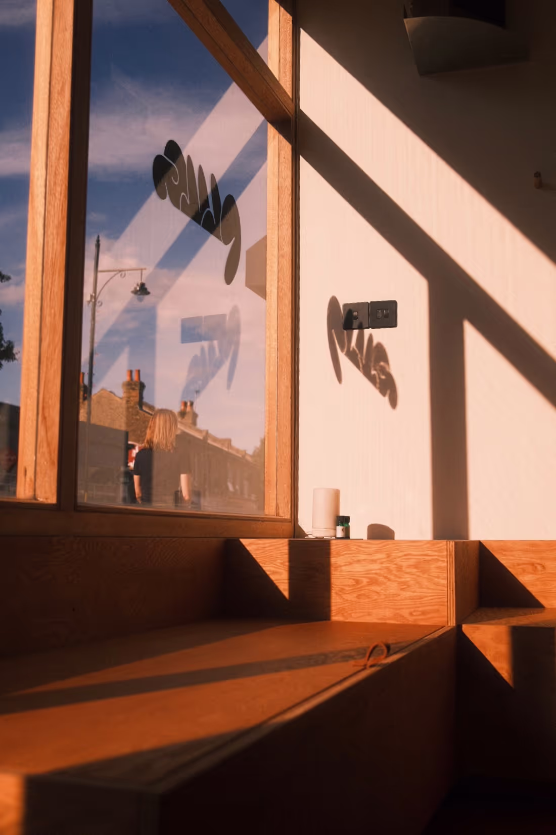 A photo of Plug London's Nunhead glass front taken from inside the salon. The shadow of Plug's logo on the glass front is cast on the wall inside.