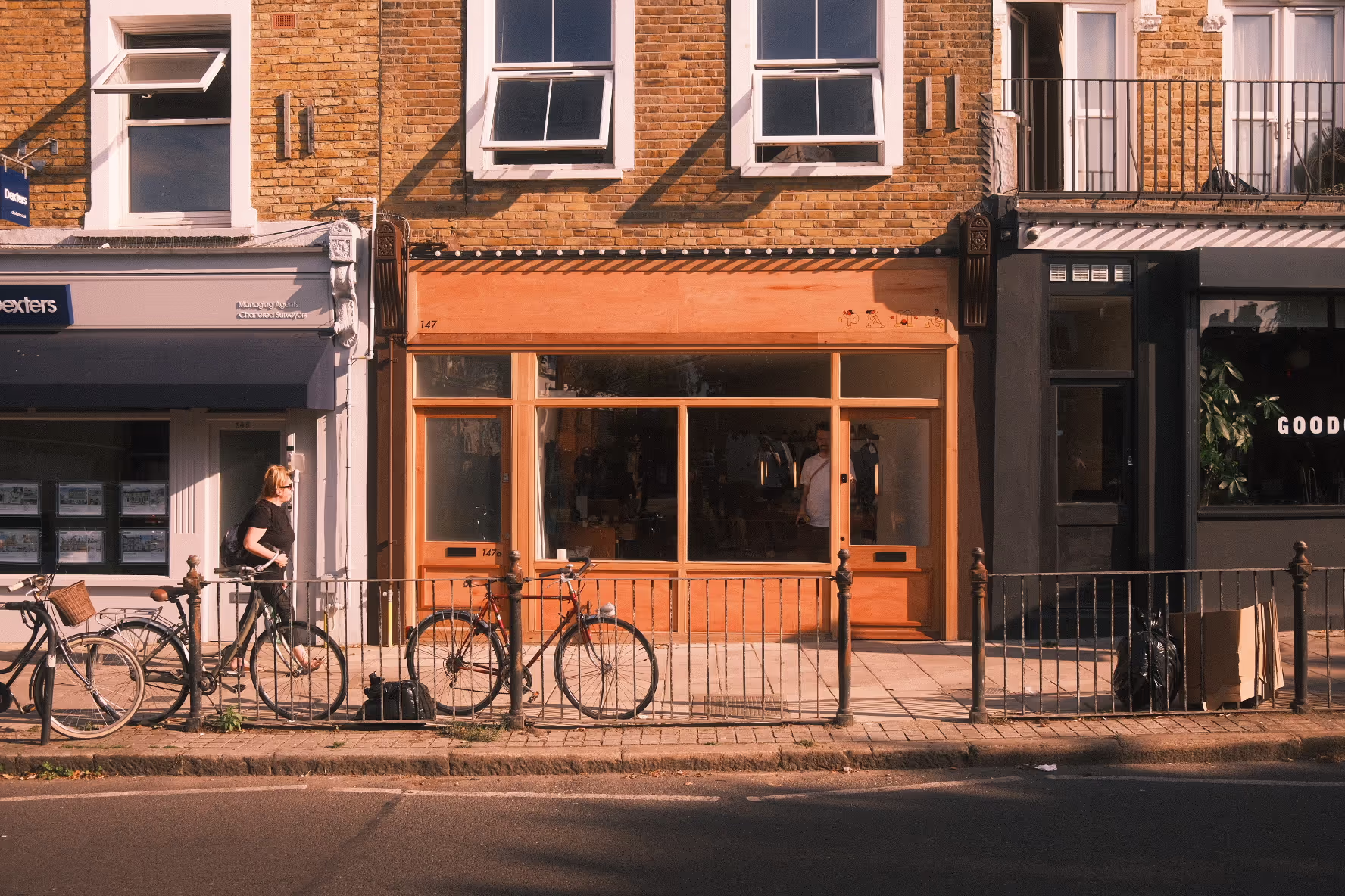 A photo of Plug London's Nunhead hair salon taken from across the street. The hair salon has a big open glass front with light orange painted front.