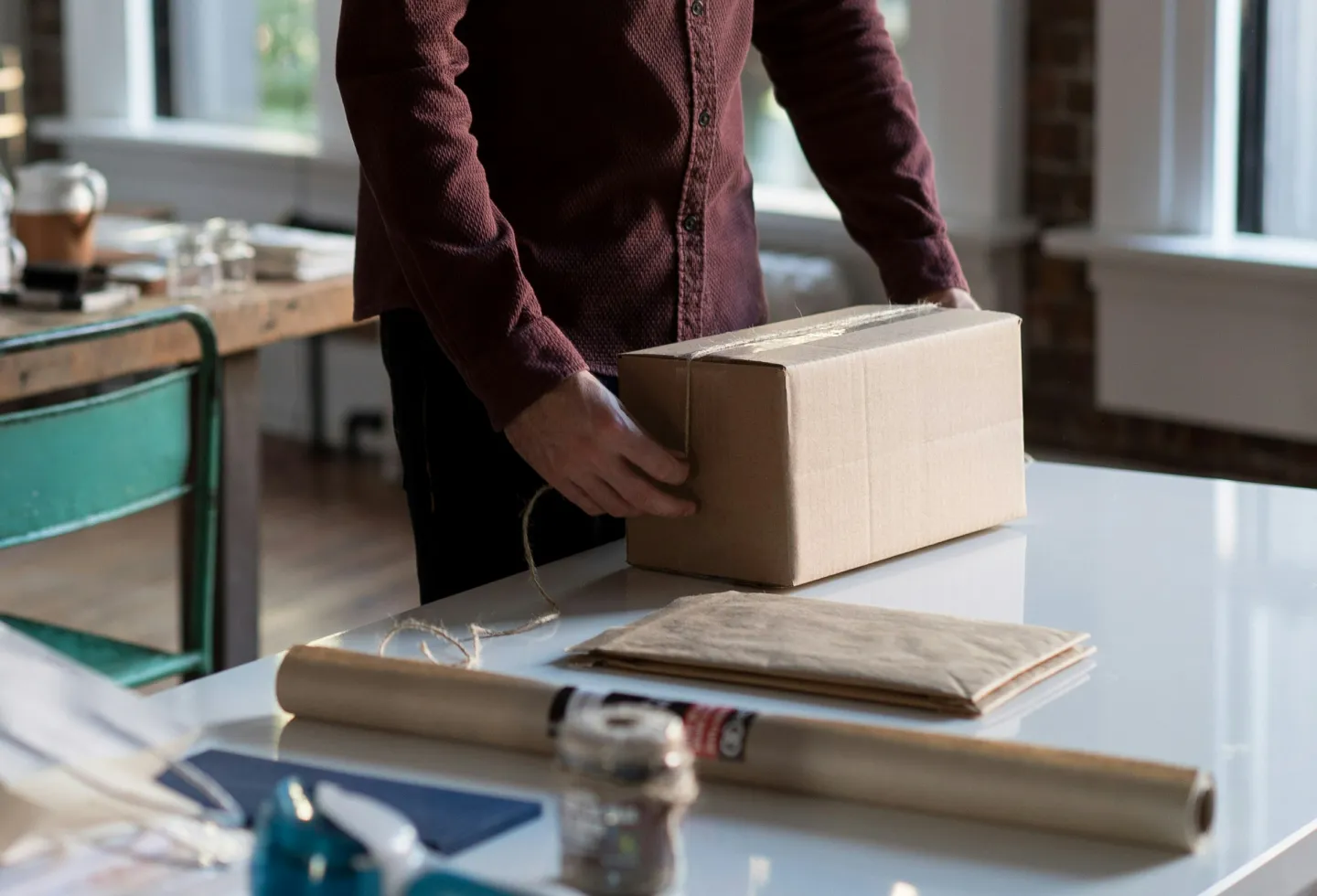 A person packing a cardboard box with twine on a white desk.