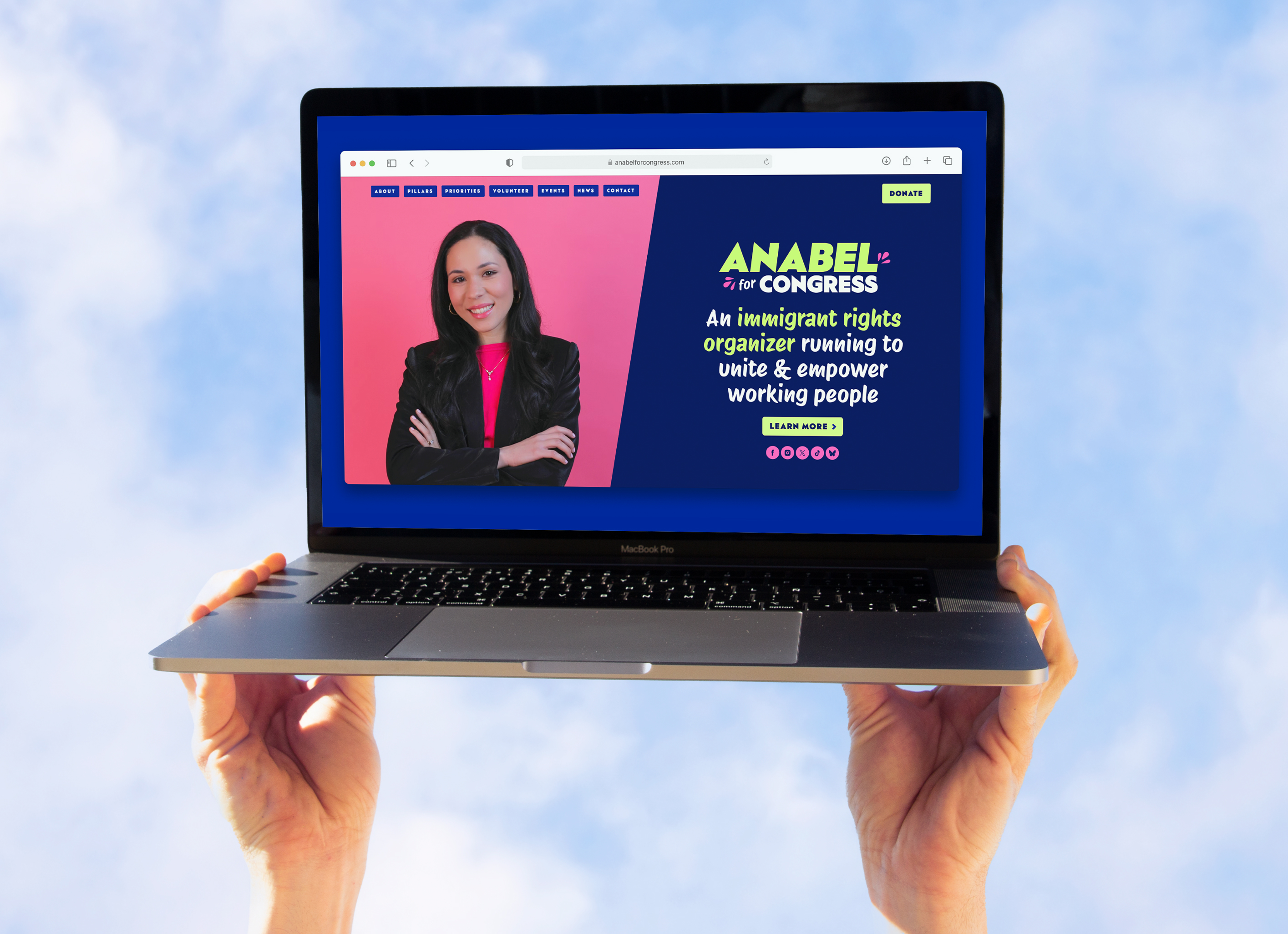 Mockup of the Anabel for Congress home page displayed in a Safari browser on a MacBook held aloft against a partly cloudy blue sky by a pair of hands.