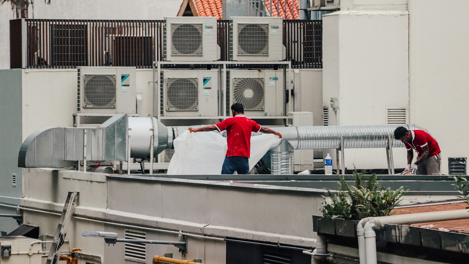 Maintenance technicians working among rooftop HVAC condensers and ductwork on a commercial building