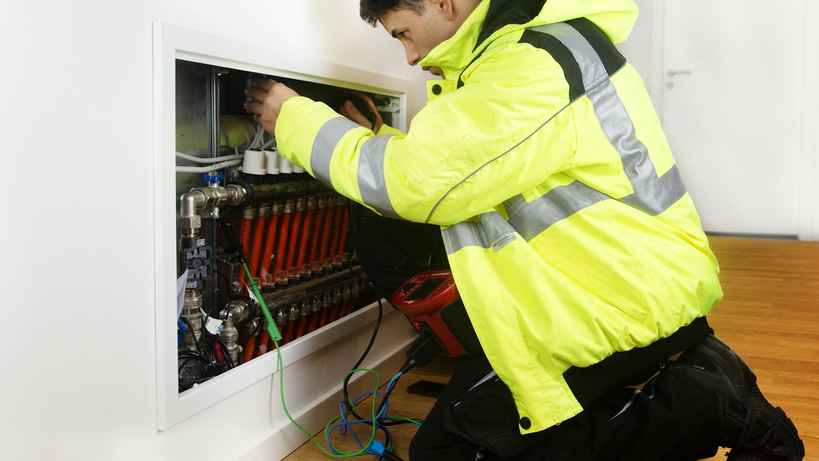 Building services engineer in hi-vis testing a heating manifold with a meter