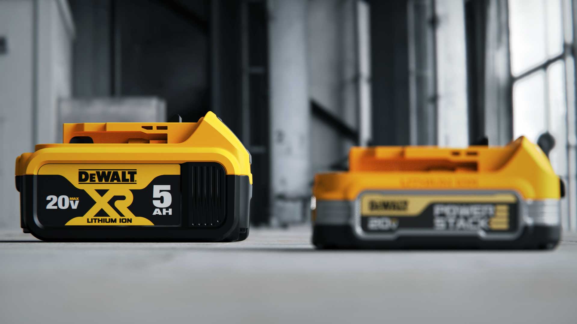 Close-up of two yellow and black DeWalt 20V XR lithium-ion power tool batteries on a concrete floor in an industrial setting.