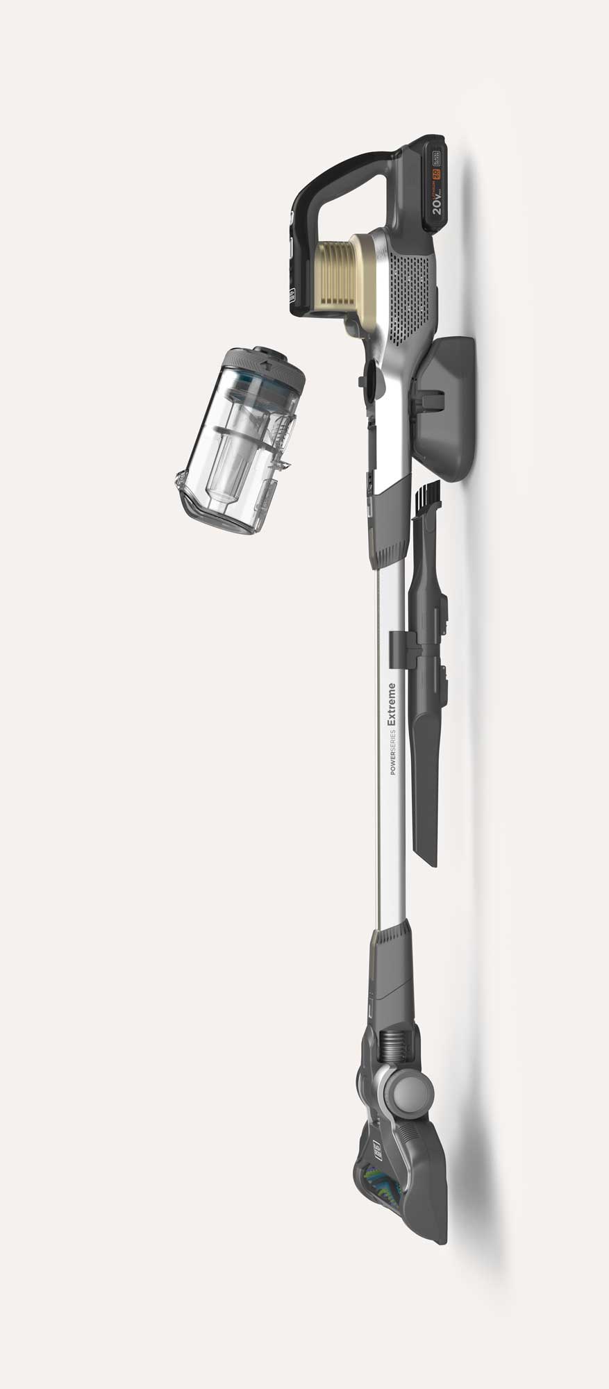 Cordless stick vacuum cleaner mounted on a wall with a detachable clear dustbin floating beside it and two cleaning attachments held on the mounting.