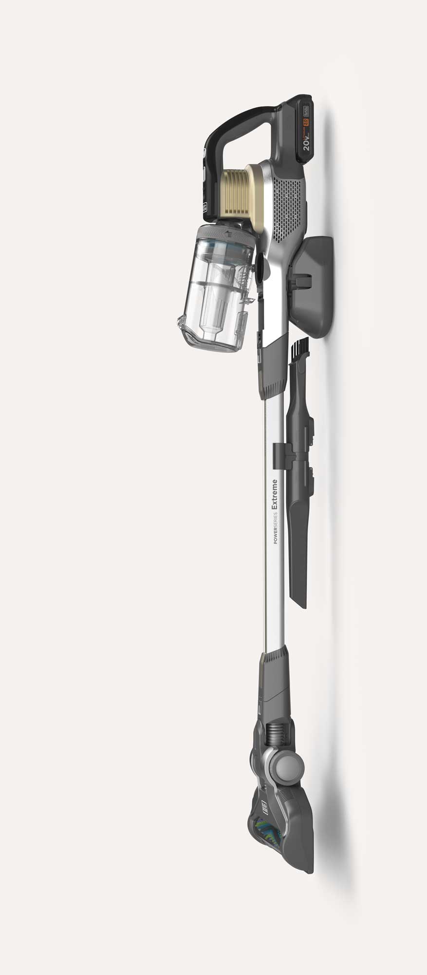 Cordless stick vacuum cleaner mounted on a wall charger, featuring a transparent dustbin, black and silver body, and a detachable cleaning tool attached to the side.