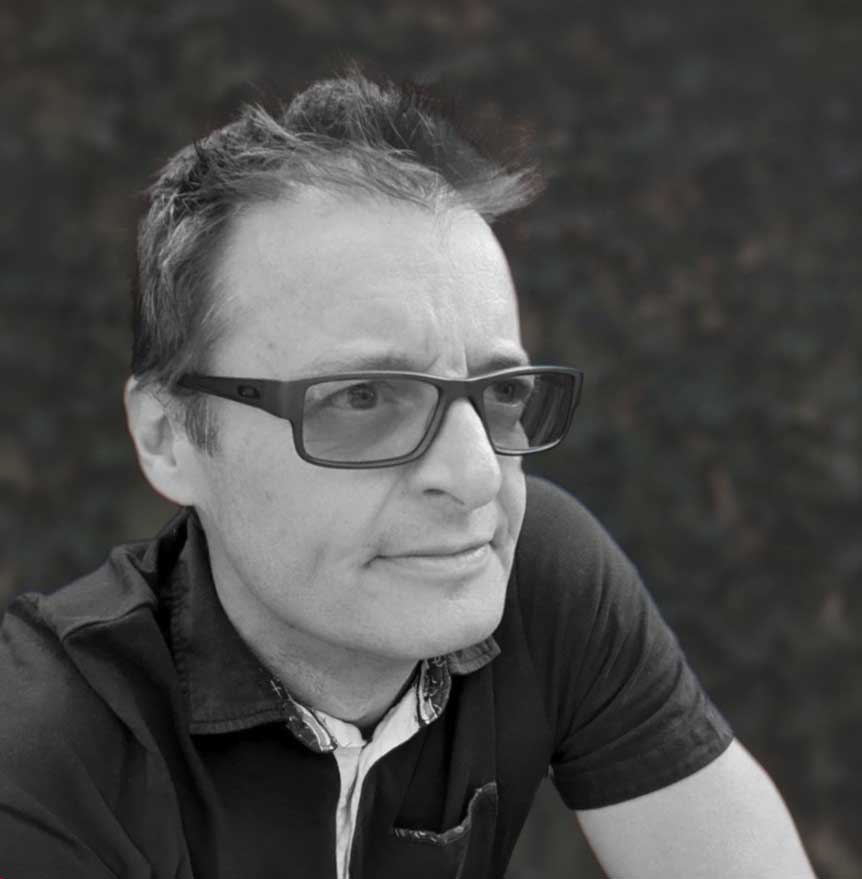 Black and white close-up photo of a man with short hair and glasses looking slightly to the right, wearing a button-up shirt with a collar and a pocket.