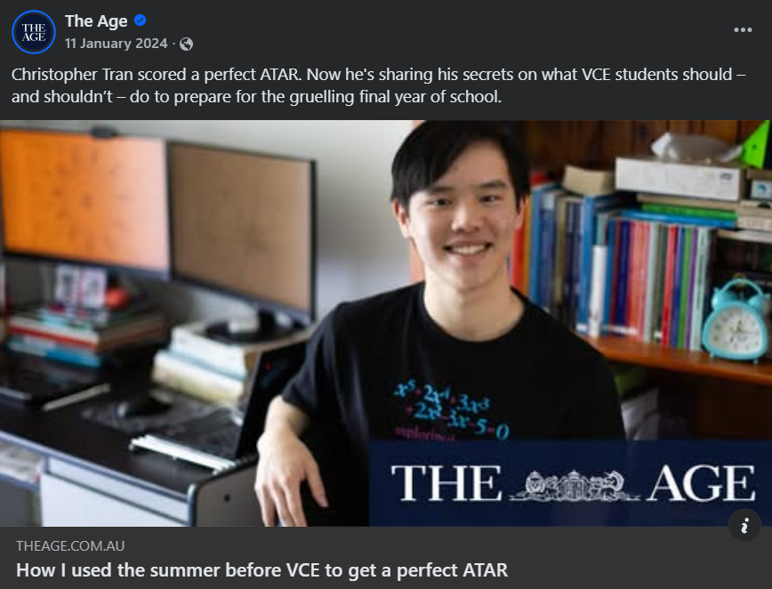 Young man smiling in a study room with books, computer monitors, and an alarm clock in the background.