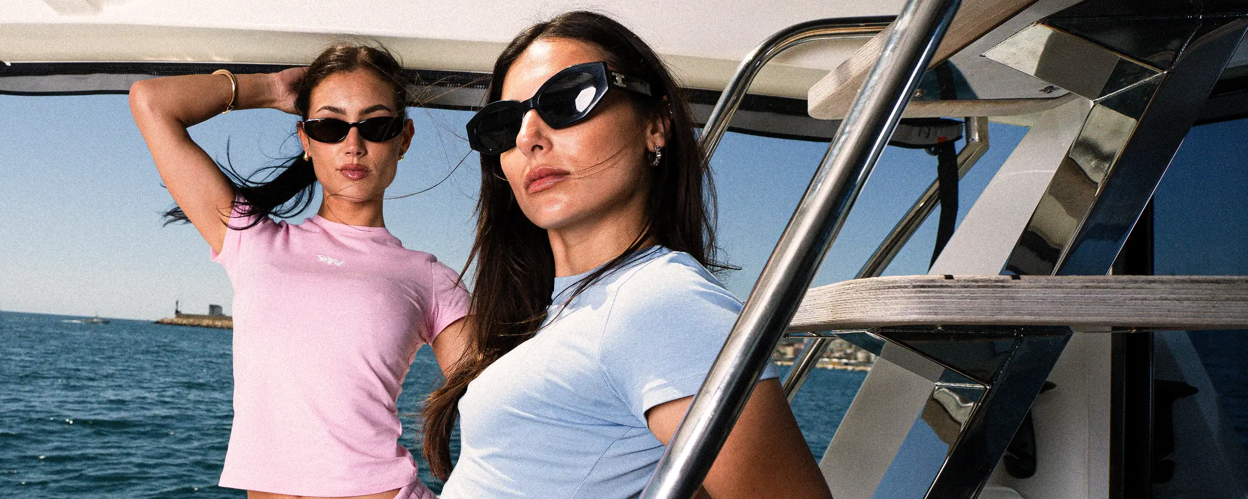 Zwei Models mit Sonnenbrillen in rosa und hellblauen 45Keys-Outfits an der Reling einer Yacht vor Mallorca.
