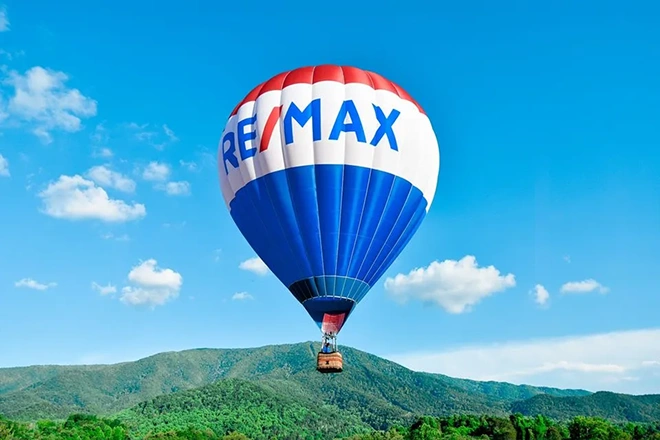 um grande balão de ar da marca Remax voa sobre os topos das montanhas verdes
