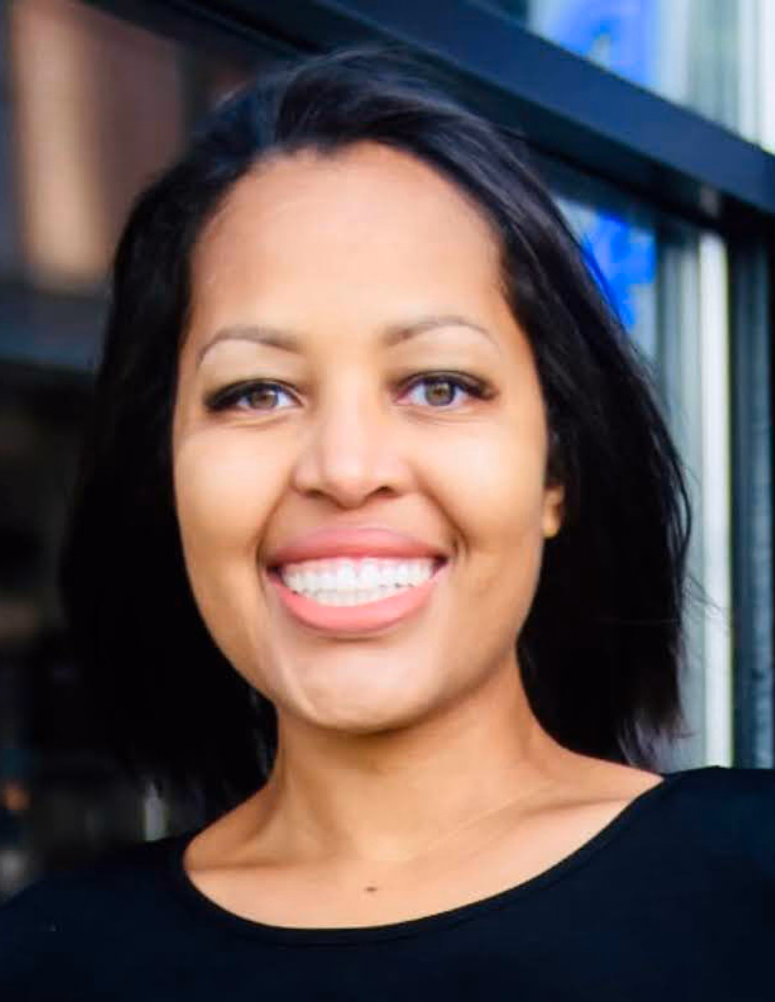 Portrait of a woman with medium brown skin, straight black hair, and brown eyes smiling while wearing a black top.