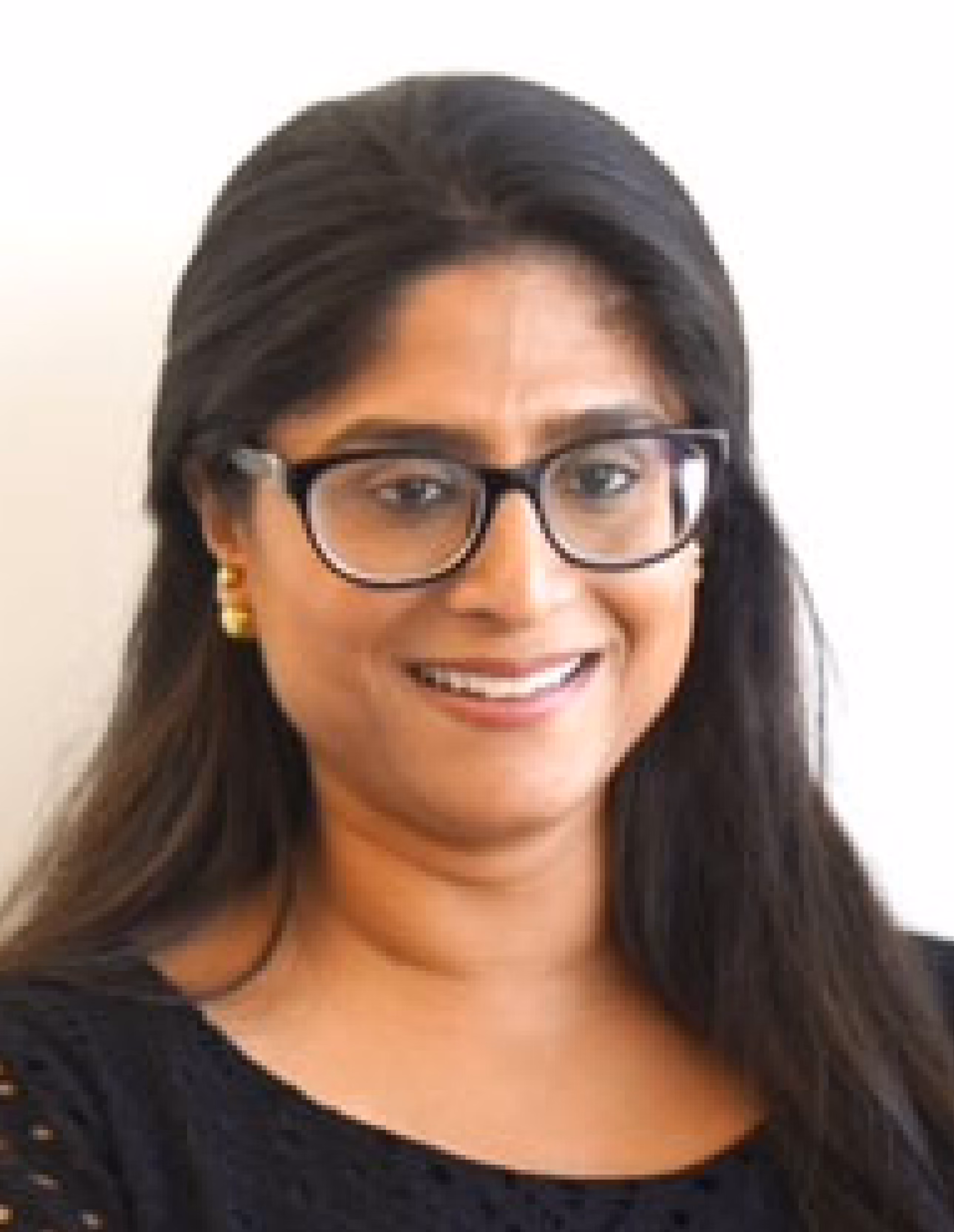 Smiling woman with long dark hair wearing black framed glasses, gold earrings, and a black top against a white background.