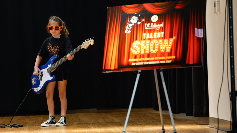DC Bilingual student performing with a guitar at the school talent show.