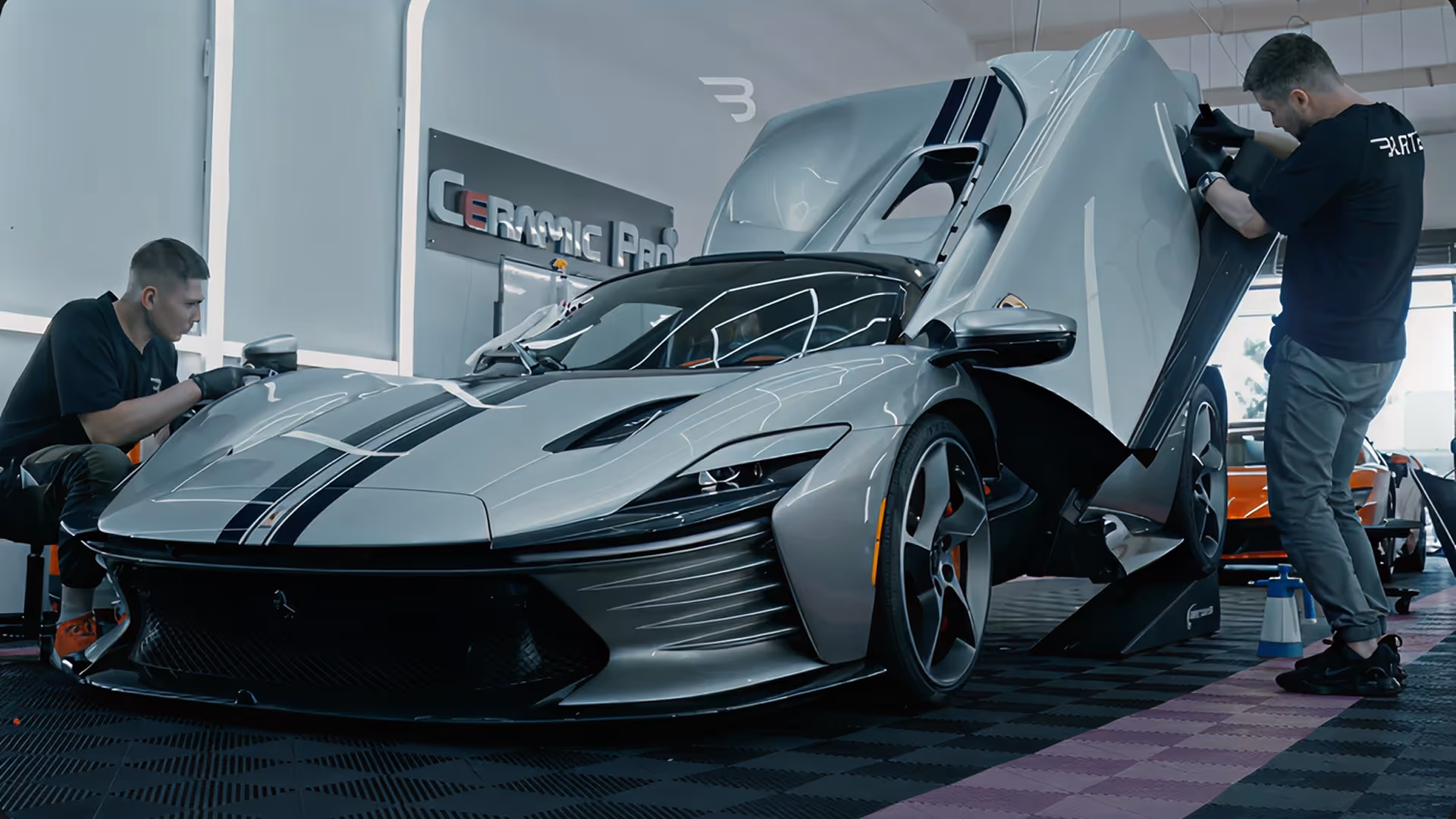 Two men working on a sleek silver sports car with butterfly doors open in a garage.