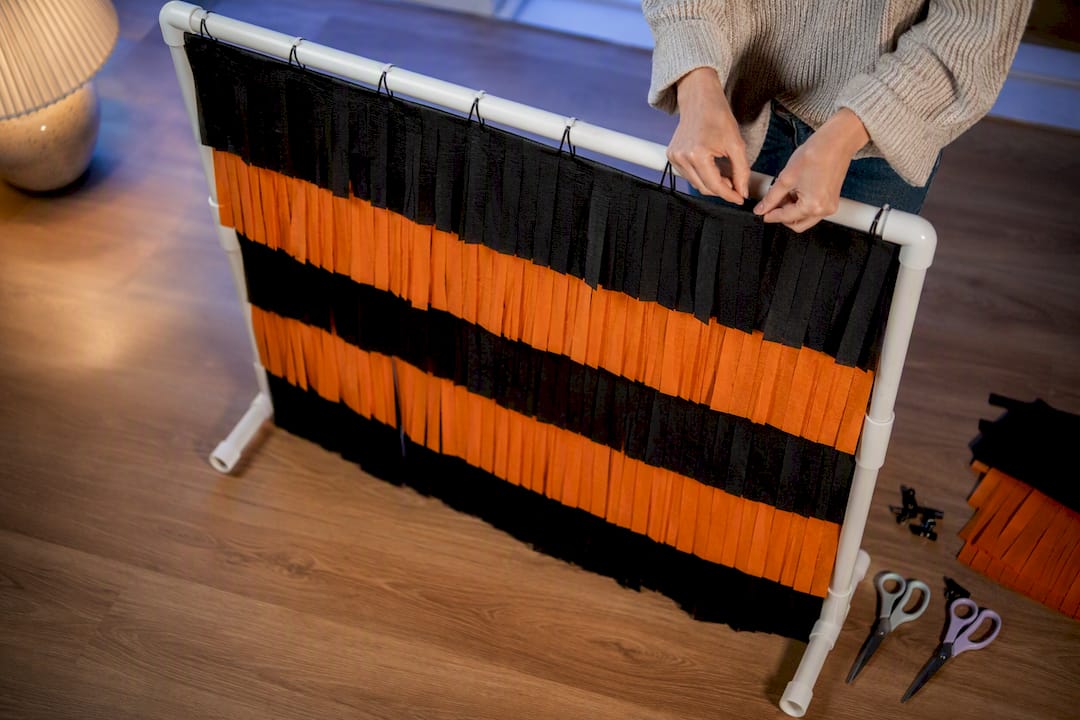 Hands attaching layered fringe to backdrop frame