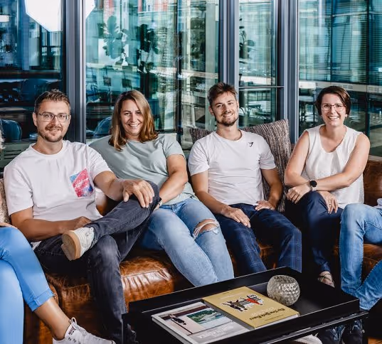 Coup Sieben team members sitting on a brown leather couch in a modern office, smiling at the camera.