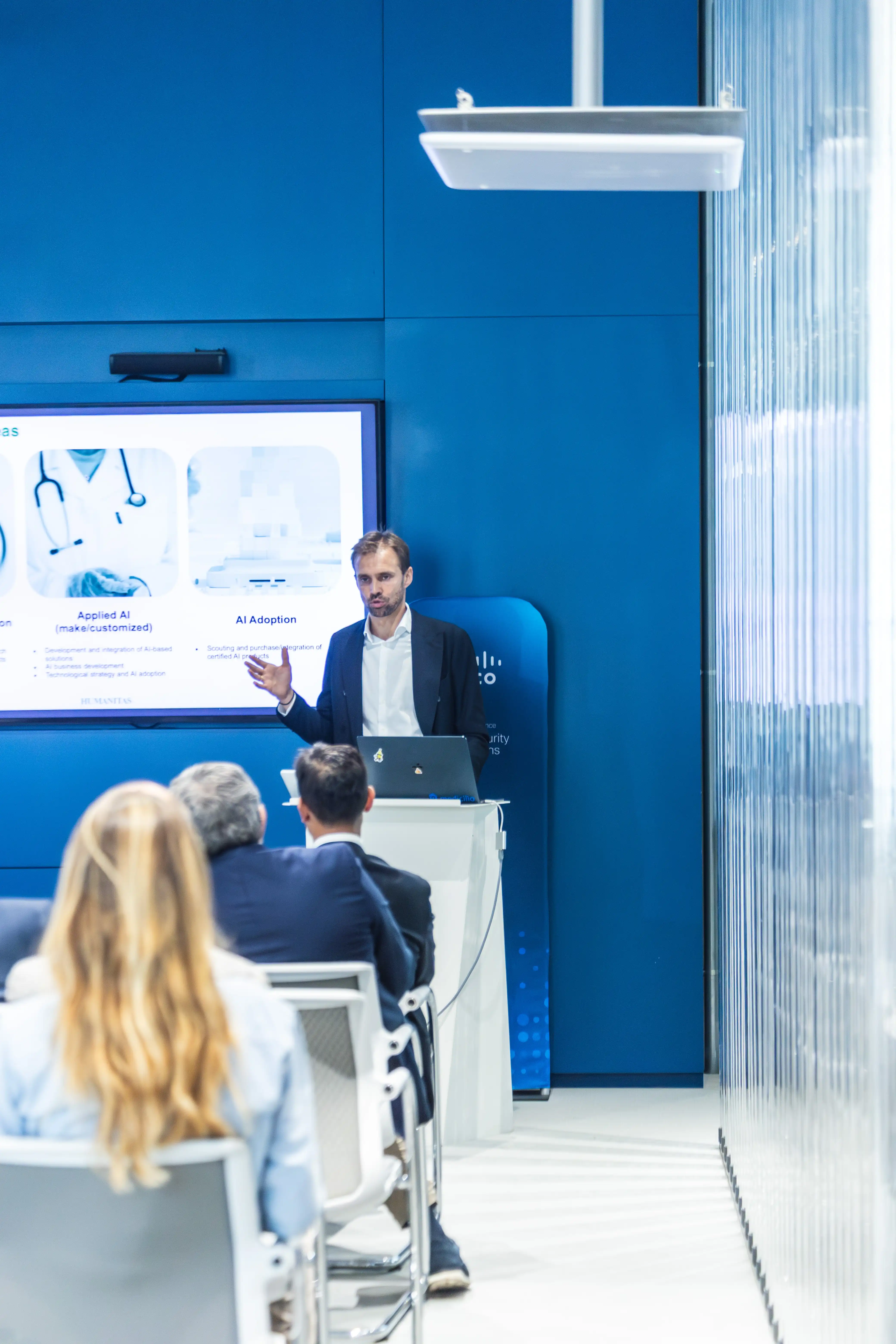 Uomo che presenta una conferenza sull'intelligenza artificiale davanti a un pubblico seduto in una sala con pareti blu.