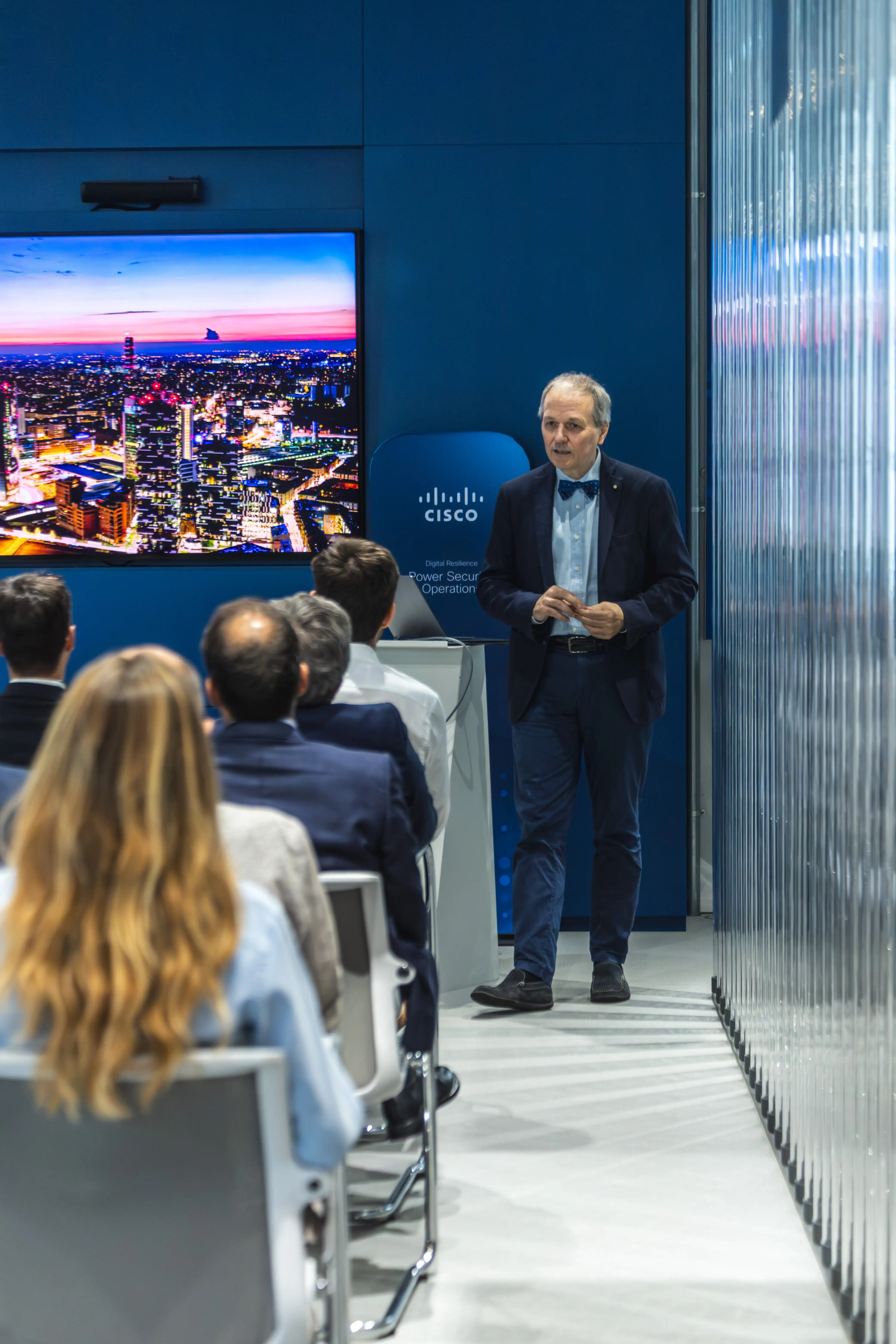 Mattia Perroni che presenta a un pubblico seduto, indicando un grande schermo con immagine di laptop.