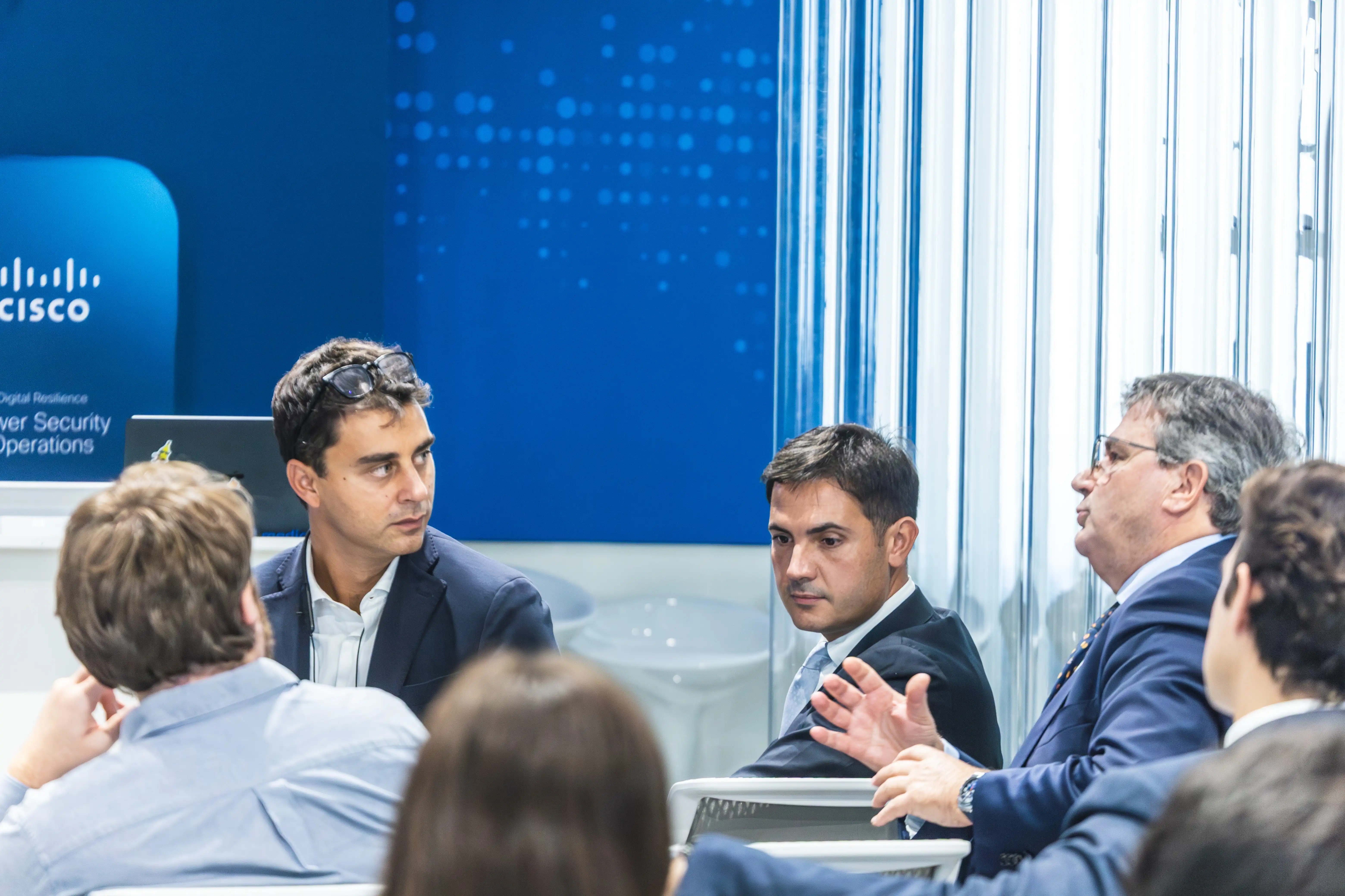 Quattro uomini in abiti formali impegnati in una conversazione durante una riunione d'affari.