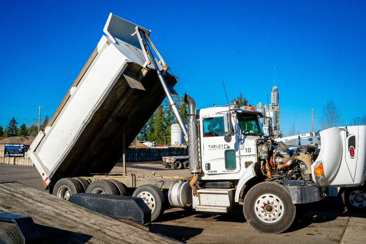 Dump truck with raised bed showing hydraulic problems during heavy-duty repair, cab labeled “Turley,” parked in yard.