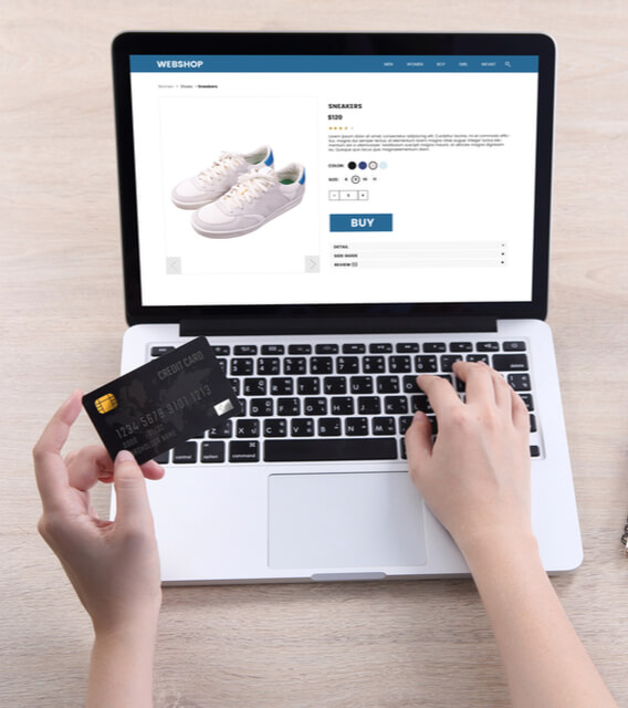 Person shopping online using a laptop and credit card, viewing sneakers on an eCommerce website checkout page.