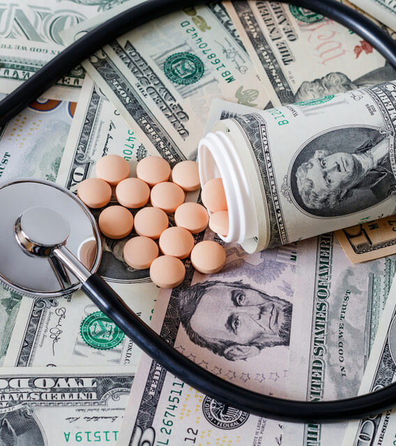 Stethoscope and pill bottle with tablets placed on U.S. dollar bills, representing healthcare costs, medical finance, and pharmaceutical expenses.