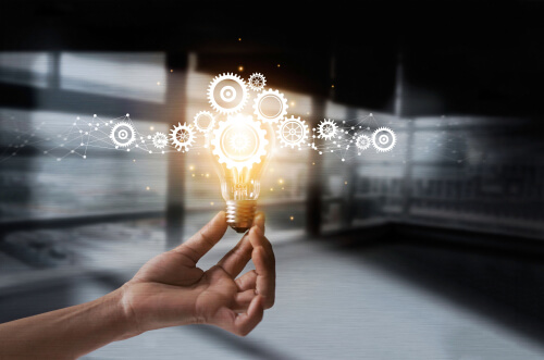 A hand holding a glowing lightbulb with digital gears and network graphics, symbolizing customized business solutions and innovative approaches.
