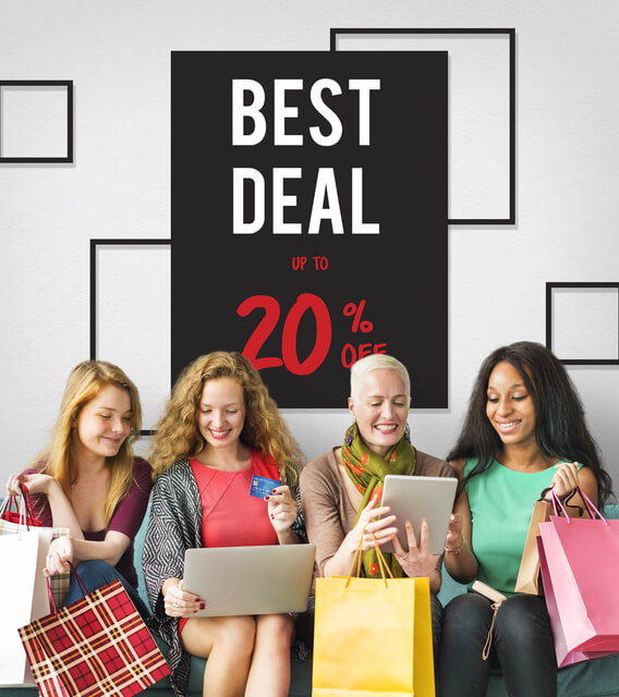 Women shopping online during a sale, holding bags and devices under a “Best Deal up to 20% Off” sign.