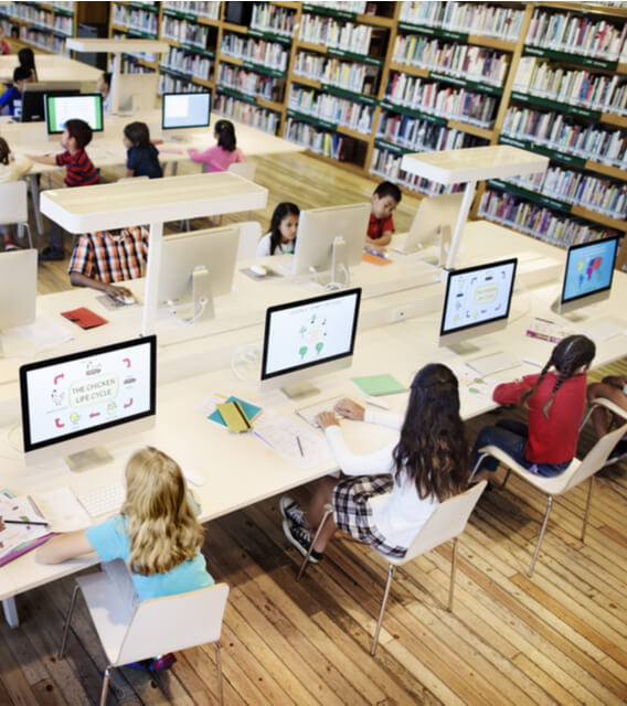 Children studying on desktop computers in a modern library or classroom, representing digital learning and educational technology.