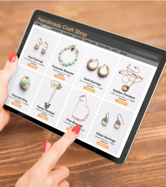 Person shopping online for handmade jewelry on a tablet displaying a craft store’s product listings.