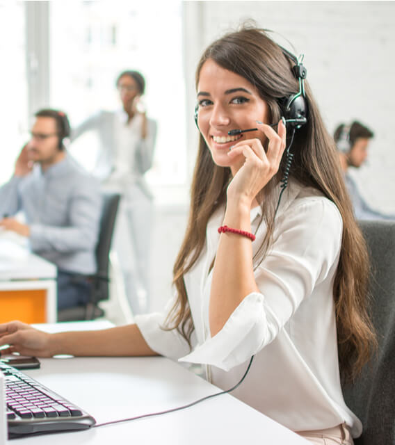 Smiling female customer support agent wearing a headset, assisting clients in a modern call center environment.