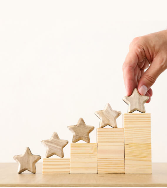 Hand placing wooden star on stacked wooden blocks to represent performance improvement and rating growth.
