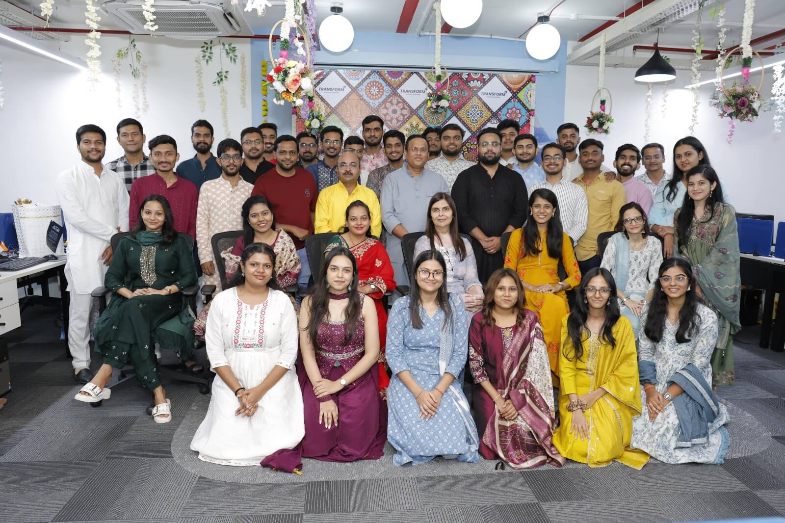 Employees at TRANSFORM Solutions posing together in traditional attire during a festive celebration at the workplace.