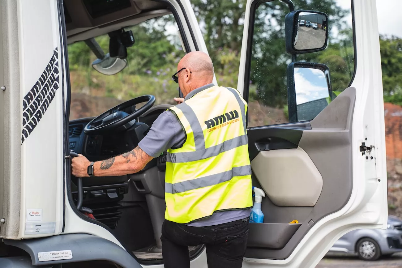 AMW Couriers driver in hi-vis vest boarding a freight truck cab ready for a driver cover shift