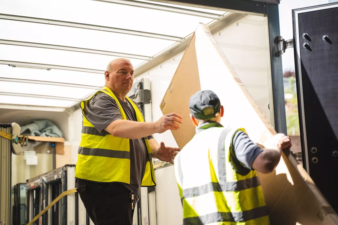 Two AMW Couriers drivers loading a large parcel into a delivery van for a multi-drop route
