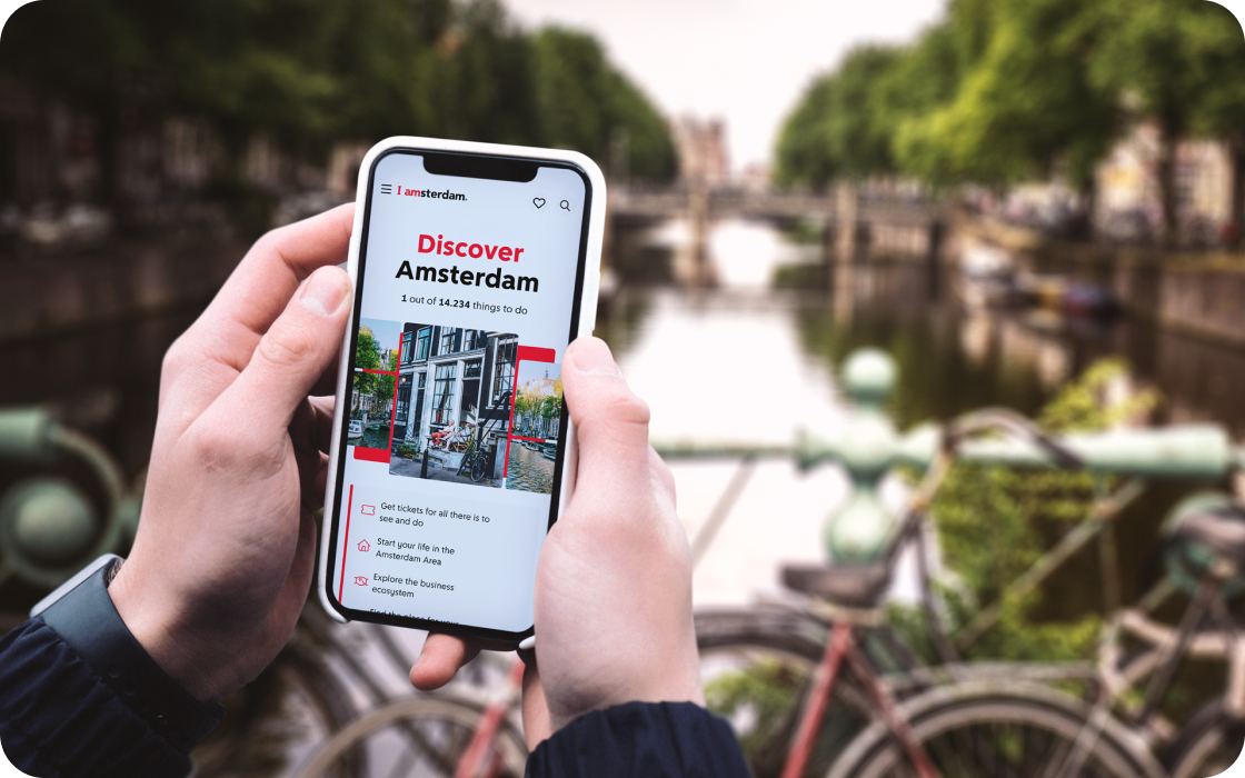 twee handen die een smartphone vasthouden met de website en een gracht op de achtergrond