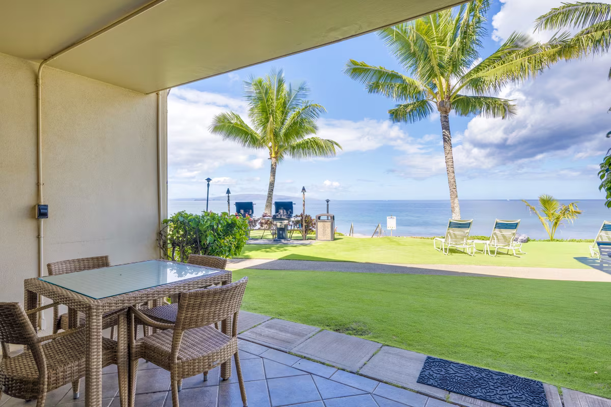 Lanai dining table looking across the oceanfront lawn and barbecue area to the beach at The Hale Pau Hana, Kihei, Maui